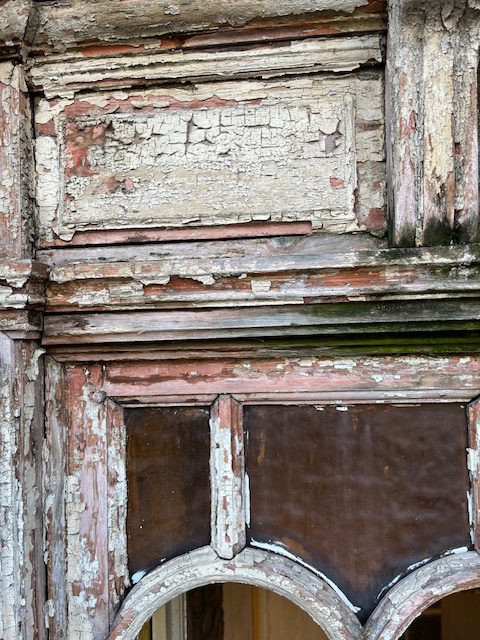 "Detail of an old wooden window frame with peeling and flaking paint, exposing bare wood and multiple layers of previuous coatings."