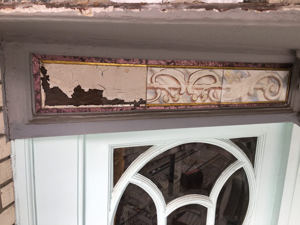 Full view of a hand-painted Art Nouveau glass panel in a pink and gilt frame, with faded scrollwork and floral motifs visible across the etched surface.