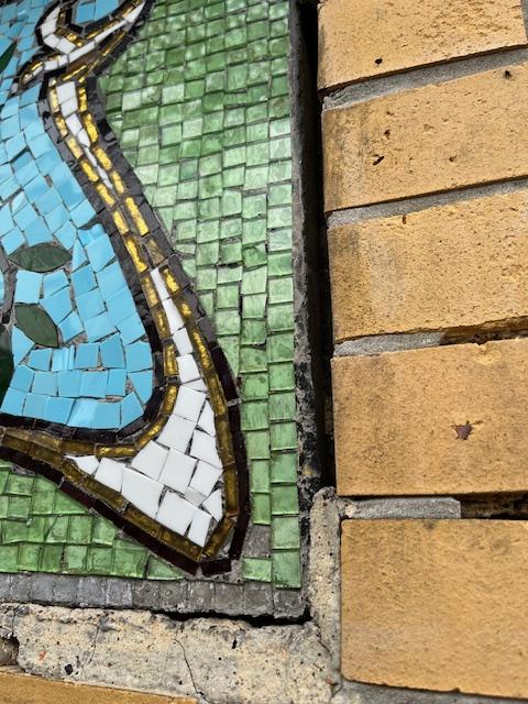 Close-up of an Art Nouveau mosaic medallion on the facade of Jaak de Braeckeleerstraat 8, showing a hot air balloon design in turquoise, purple, and ochre glass tesserae, framed by painted floral scrollwork.