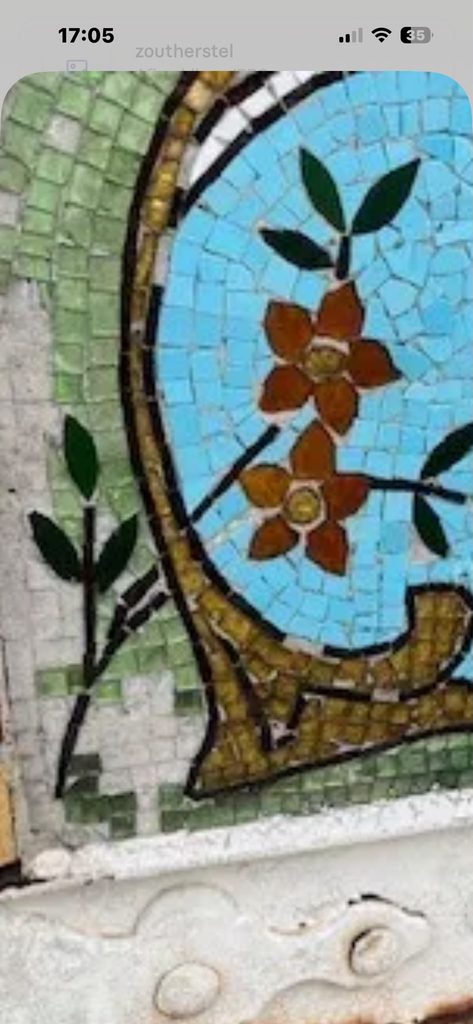 Close-up of mosaic tesserae loss, showing missing green glass pieces alongside intact enamel tesserae in the same panel, exposing the bare mortar bed beneath.